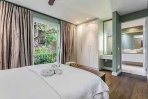 A bedroom with a bed, a bench, a mirror, and a view of greenery outside. - Spacious spectacular 9-bedroom Fresnaye Villa (Cape Town)