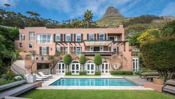 Ein modernes, zweistöckiges Haus mit Schwimmbad, umgeben von Grünflächen und einer hügeligen Landschaft.