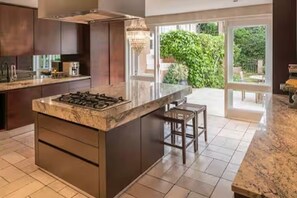 A modern kitchen with a central island, dark cabinetry, and a view to a garden through glass doors. - Spacious spectacular 9-bedroom Fresnaye Villa (Cape Town)
