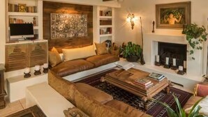 Ein Wohnzimmer mit einem braunen Ledersofa, einem Couchtisch mit Büchern, einem Kamin und einem an der Wand montierten Fernseher.