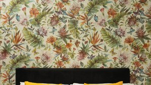 Una cama con ropa de cama blanca y dos almohadas amarillas, sobre un fondo de papel tapiz floral.