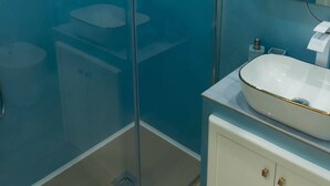 Un baño con cabina de ducha de vidrio, un lavabo blanco con detalles dorados y un mueble con tiradores dorados.