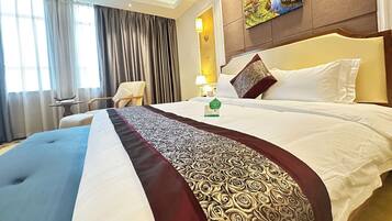 A hotel room with a large bed, a chair, a table, and a painting on the wall.