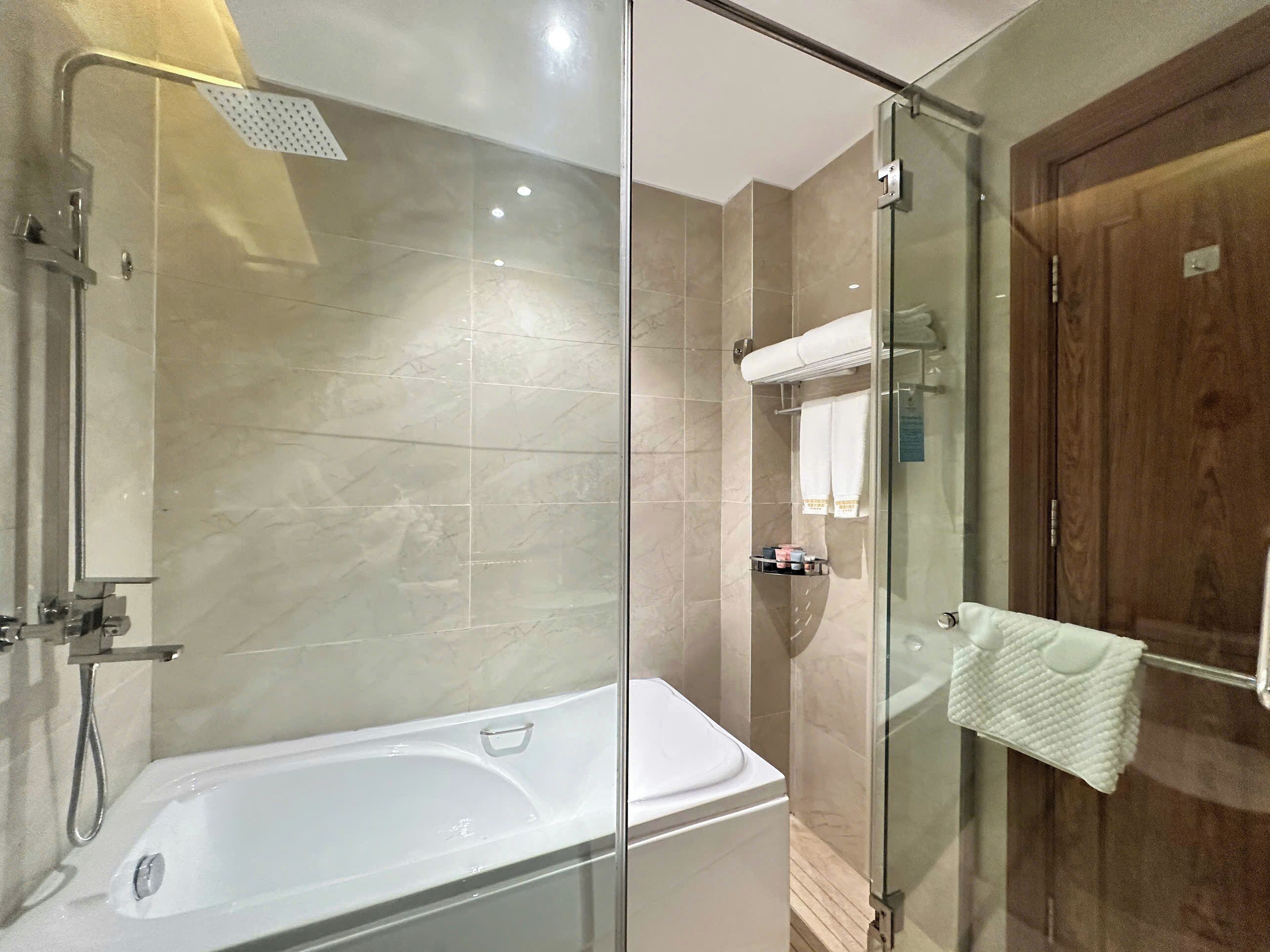 A modern bathroom with a glass-enclosed shower, a white bathtub, and a wooden door.