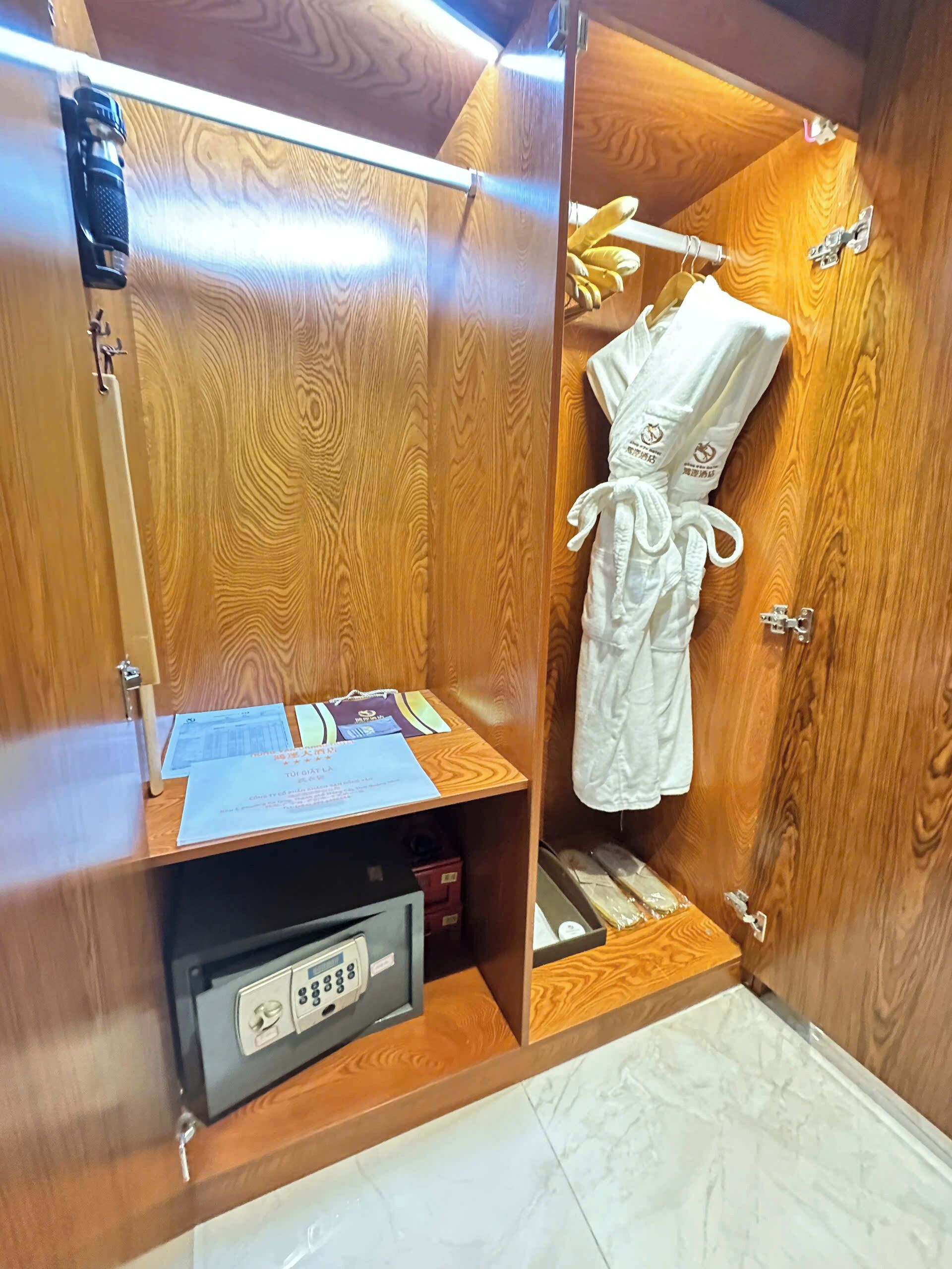 A wooden wardrobe with a mirror, a white robe, and a small safe.