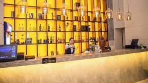 Uma área de bar com um bartender, prateleiras com garrafas de bebidas e luminárias pendentes.
