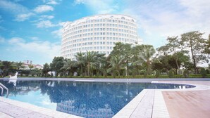 Um hotel grande e moderno com design circular, piscina e vegetação ao redor.