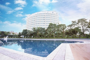 Un hotel gran i modern amb disseny circular, una piscina i vegetació circumdant.