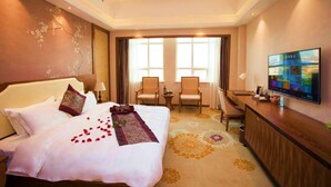 Quarto de hotel com cama, duas cadeiras, escrivaninha, televisão e uma grande janela.