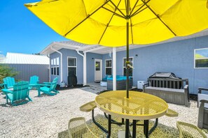 Eine Terrasse mit Gartenmöbeln, einem gelben Sonnenschirm und einem Grill.
