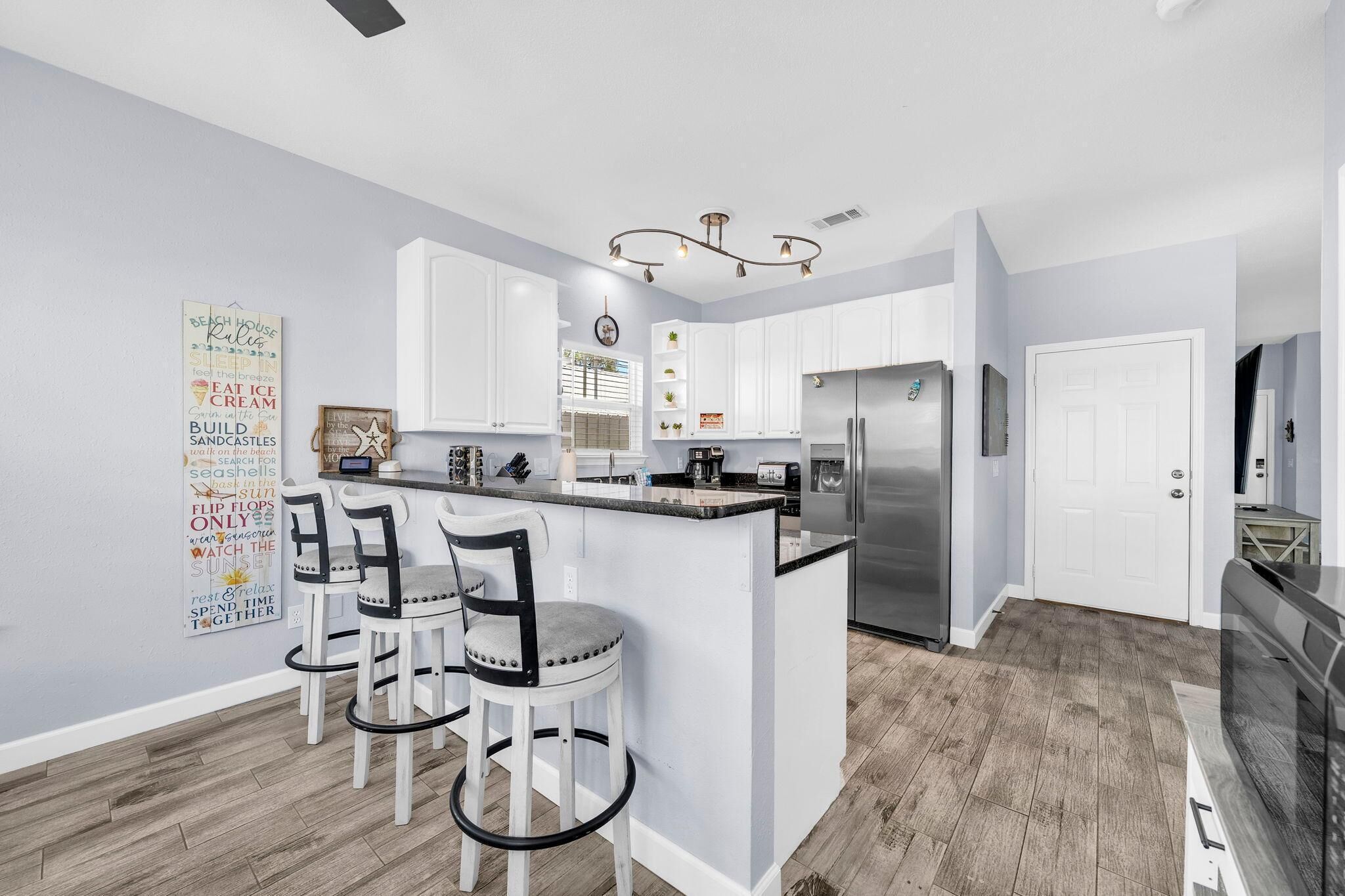 A modern kitchen with white cabinets, a stainless steel refrigerator, and a bar area with stools.