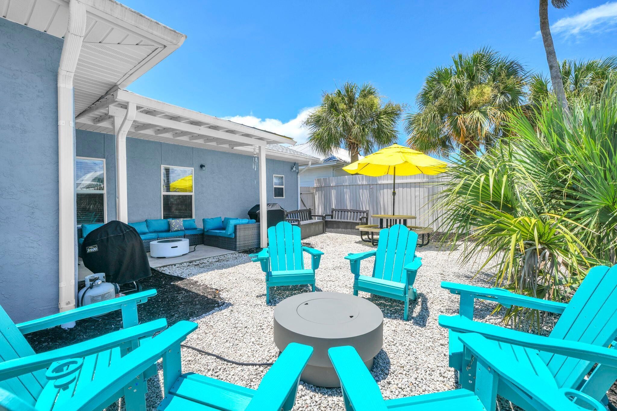 An outdoor patio area with turquoise Adirondack chairs, a round table, and a yellow umbrella.