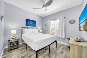 Une chambre à coucher avec un lit, un ventilateur de plafond, une fenêtre avec des rideaux, une décoration murale en forme d’étoile de mer et un tableau représentant une tortue de mer.