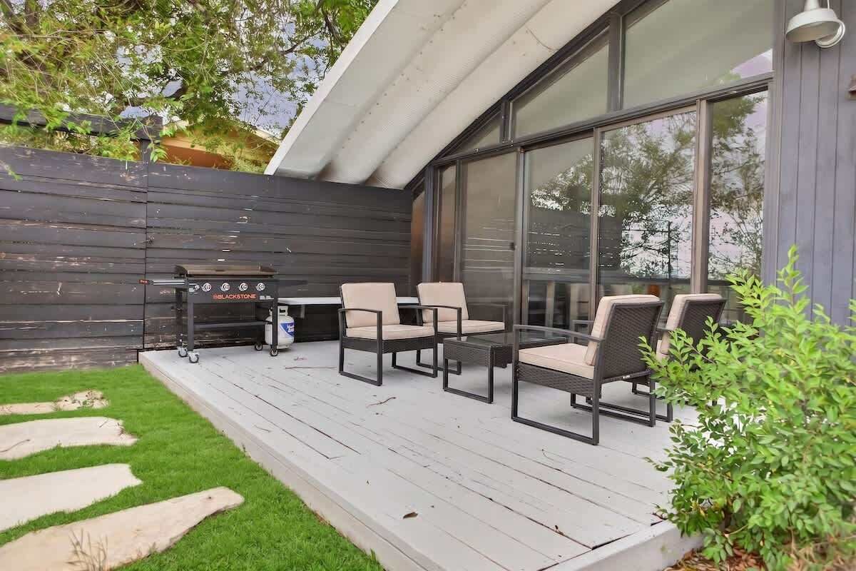 Eine Terrasse mit Gartenmöbeln, einem Grill und einem großen Fenster.