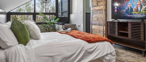 A bedroom with a bed, a TV, and a large window.