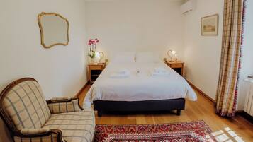 Une chambre à coucher comprenant un lit, une chaise, une table de chevet avec une lampe, un miroir et une fenêtre avec des rideaux.