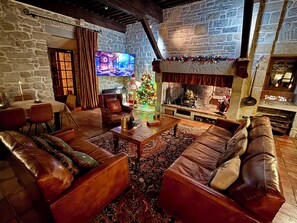 A cozy living room with leather sofas, a fireplace, a stone wall, and a Christmas tree.