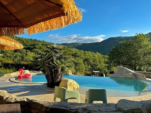 Une piscine avec un flotteur en forme de flamant rose, un palmier et une chaîne de montagnes en arrière-plan.
