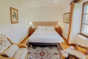 A neatly arranged bedroom with a large bed, two bedside tables with lamps, a patterned rug, and a window with curtains. - Château de Tournou – Sleeps 15, 7 Bedrooms & Private Infinity Pool (Castelreng)