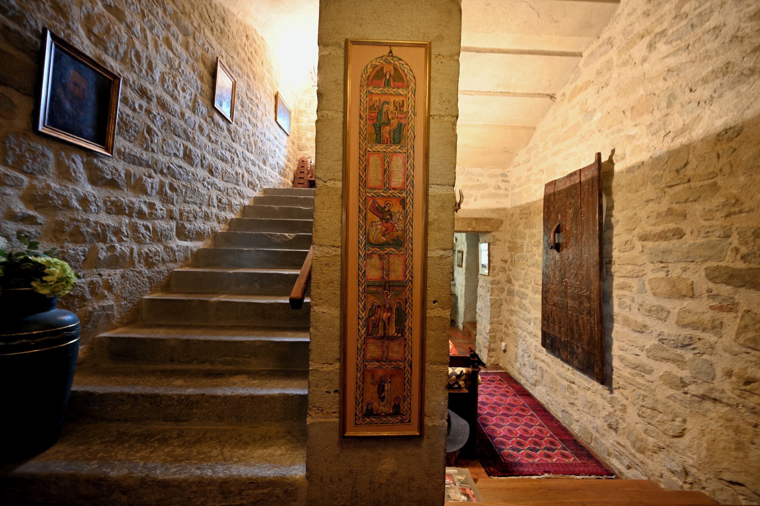 Un escalier en pierre menant à un niveau supérieur, une porte en bois ornée d’un panneau décoratif et un tapis à motifs.
