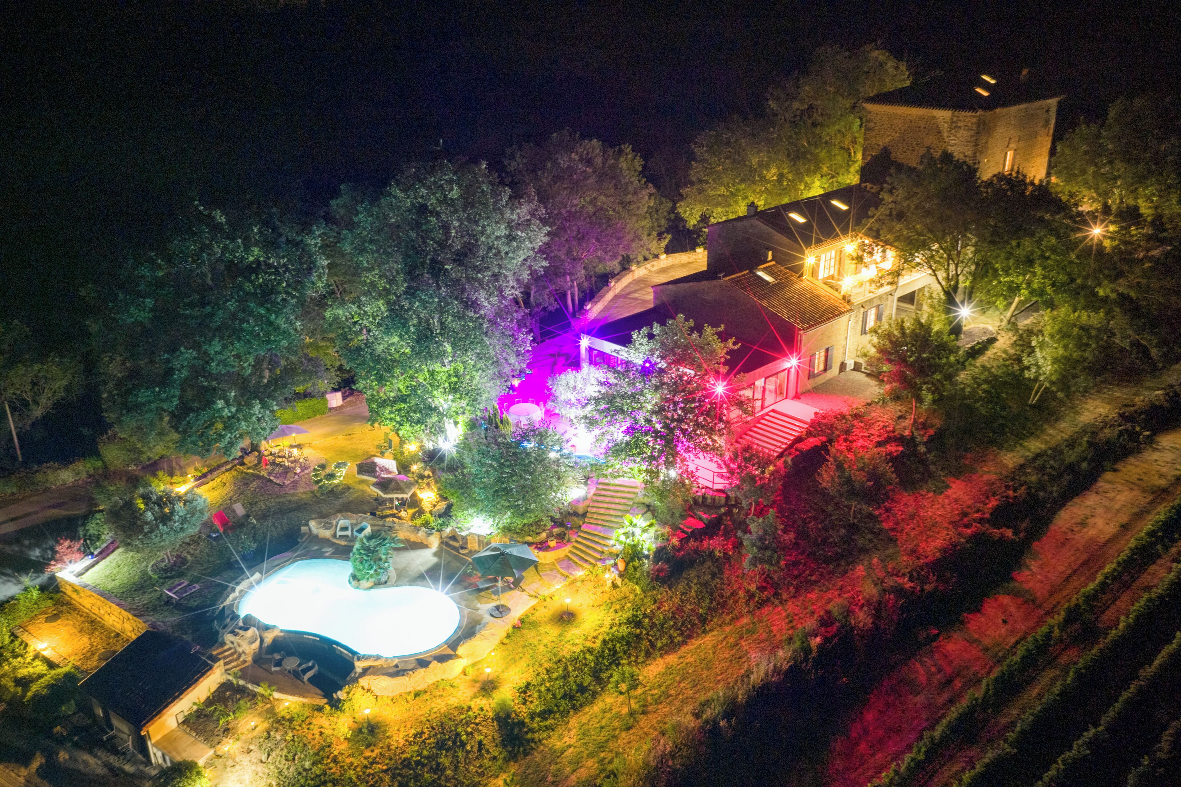 Une vue nocturne d’une propriété dotée d’une piscine, d’un espace salon extérieur et d’un bâtiment en pierre.