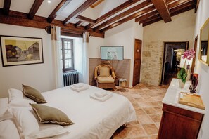 A bedroom with a large bed, a chair, a television, and a bathroom visible through an open door.