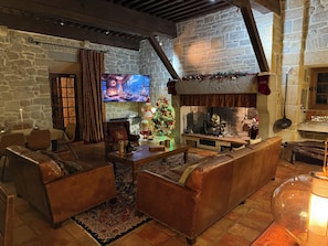 Una sala de estar acogedora con paredes de piedra, sofás de cuero, una chimenea y un árbol de Navidad.