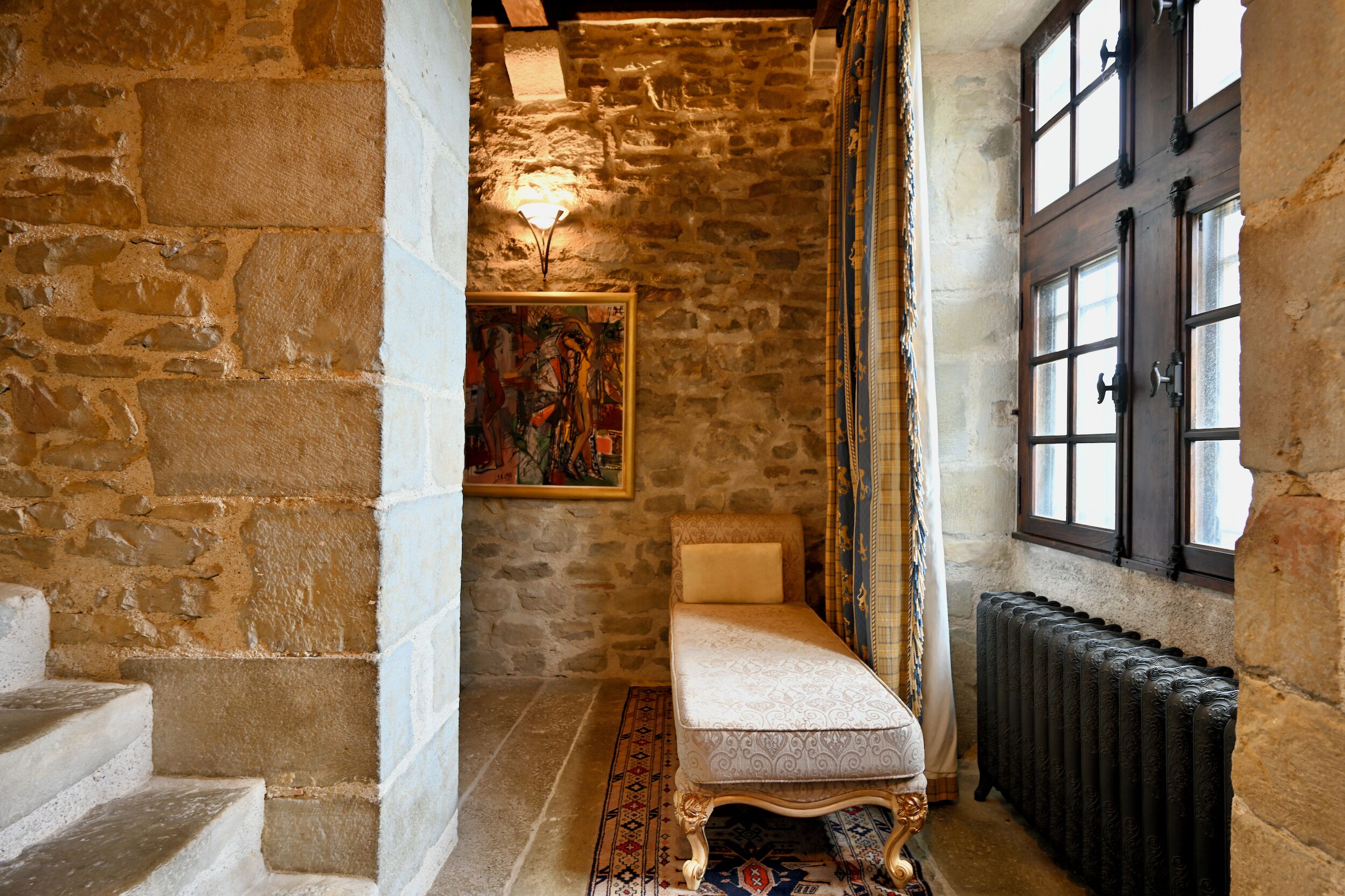 A stone-walled room with a bench, a radiator, and a window with shutters.