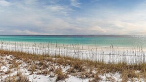 Una playa con aguas turquesas cristalinas, arena blanca y vegetación escasa.