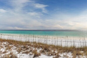 Ein Strand mit klarem türkisblauem Wasser, weißem Sand und spärlicher Vegetation.
