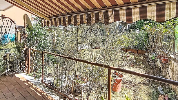 Un espace extérieur abrité, doté d’un toit à rayures, d’une clôture en métal et de diverses plantes.
