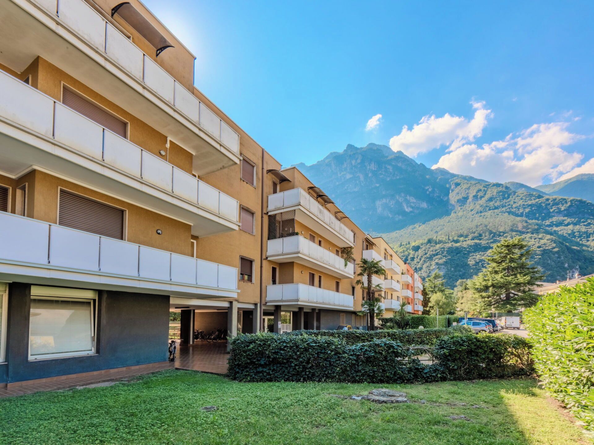 Un hotel a più piani con balconi, un'area di parcheggio e montagne sullo sfondo.