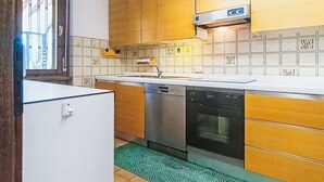 Une cuisine compacte dotée de meubles en bois, d’un évier en acier inoxydable, d’un lave-vaisselle et d’un four encastré.