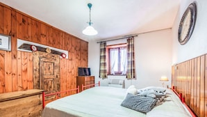 Ein Schlafzimmer mit Holzpaneelen, einem Bett mit Steppdecke, einem Fernseher, einer Uhr und einem Fenster mit Vorhängen.