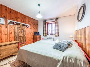 Ein Schlafzimmer mit Holzpaneelen, einem Bett mit Steppdecke, einem Fernseher, einer Uhr und einem Fenster mit Vorhängen.