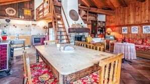 Ein rustikaler Innenraum mit einem Holzesstisch, Bänken, einem Kamin und einer gemütlichen Sitzecke.