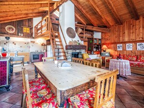 Ein rustikaler Innenraum mit einem Holzesstisch, Bänken, einem Kamin und einer gemütlichen Sitzecke.