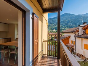 Un balcón con vistas a un paisaje montañoso, un comedor con mesa y sillas, y una puerta de madera.