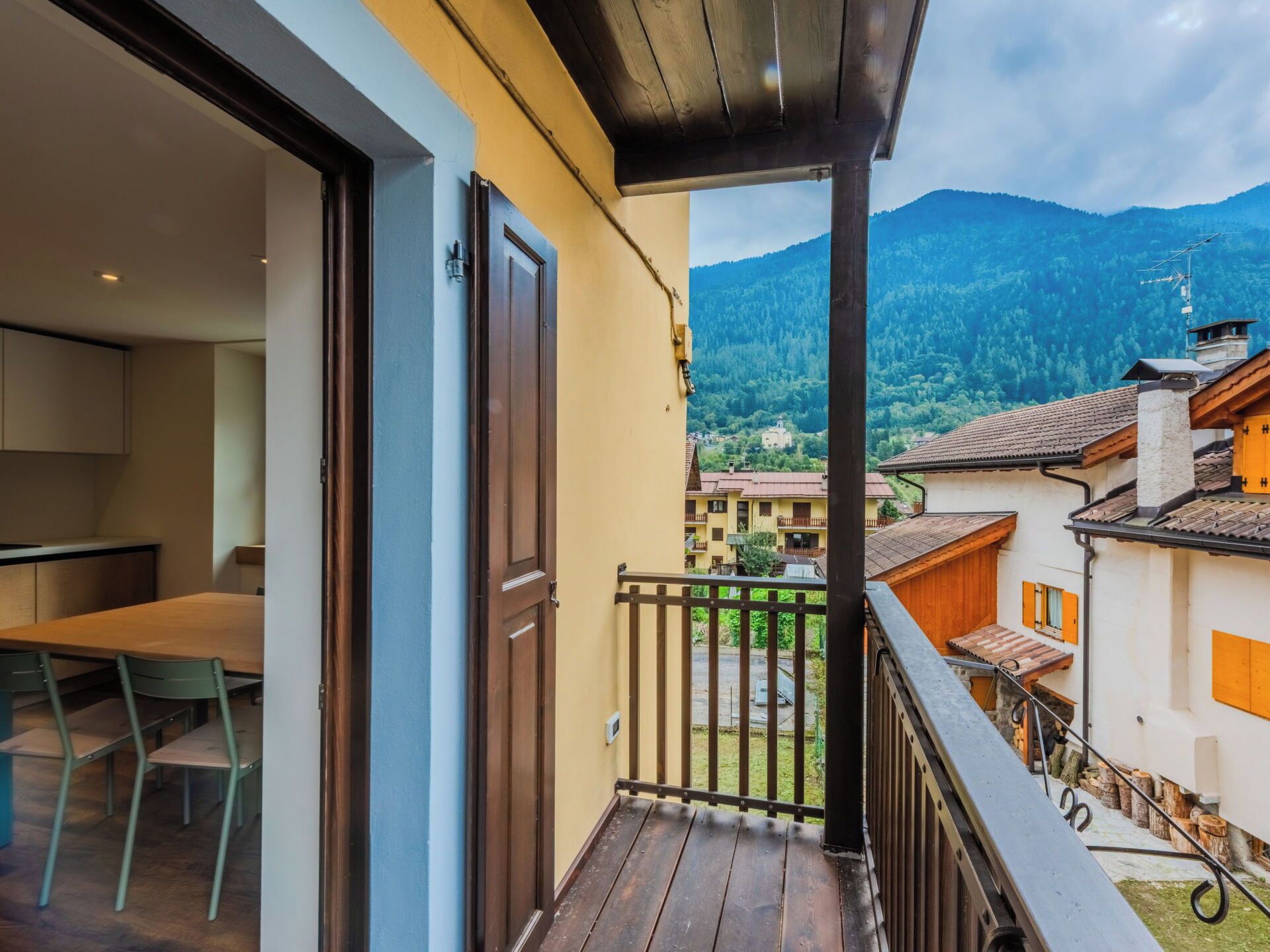 A balcony with a wooden floor and metal railing, overlooking a mountainous landscape with traditional buildings.