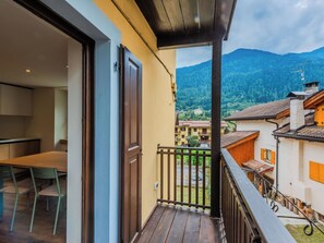 Varanda com piso de madeira e grade de metal, com vista para uma paisagem montanhosa e edifícios tradicionais.