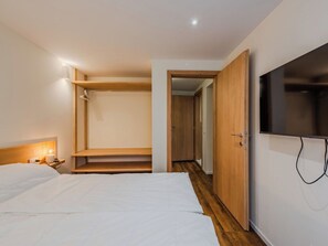 Een hotelkamer met een bed, een nachtkastje met een lamp, een houten garderobe en een televisie.