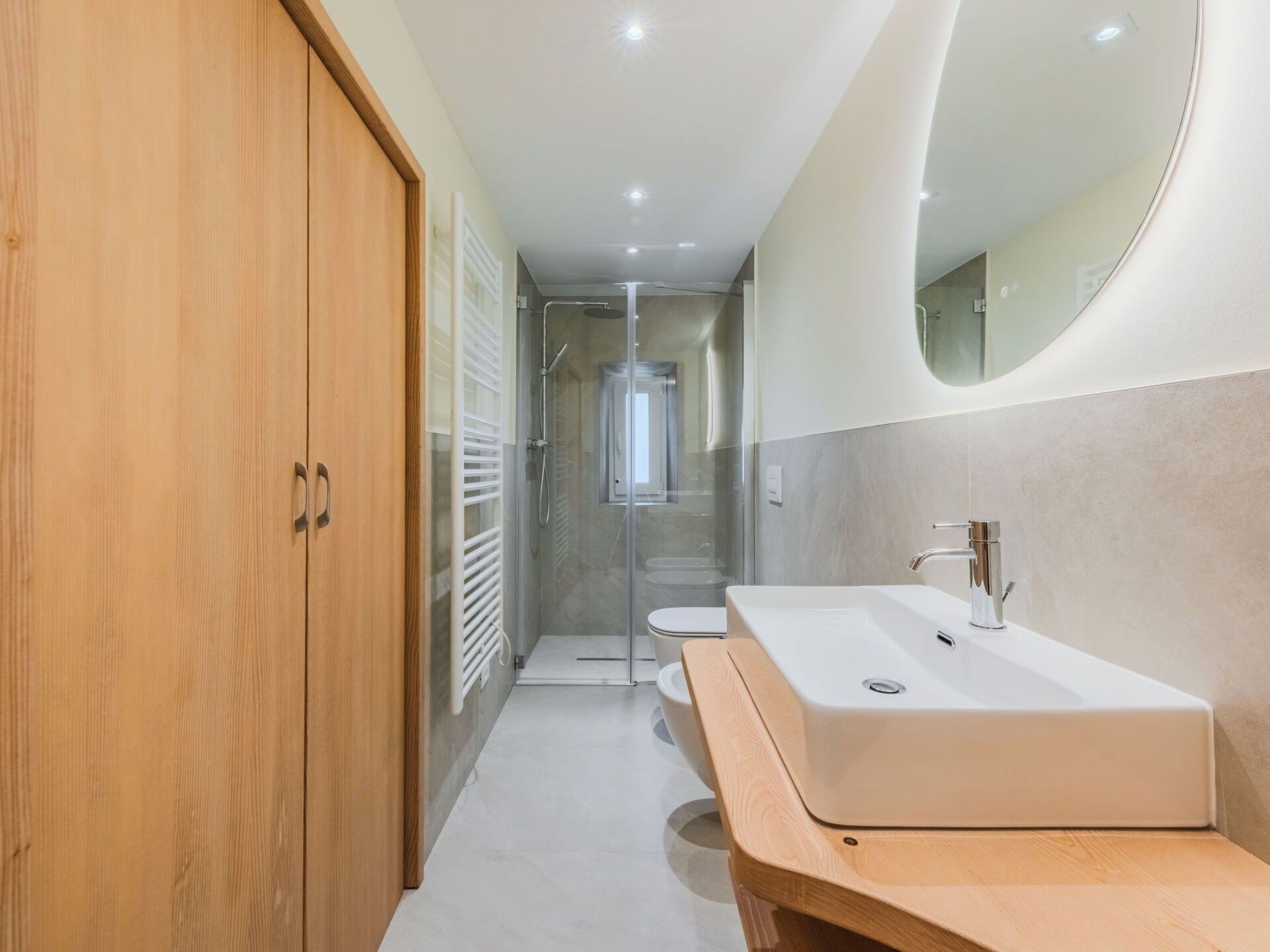 A modern bathroom with a wooden wardrobe, a large sink, and a glass-enclosed shower.