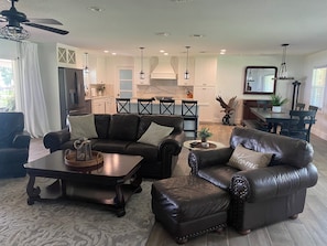 A modern living room with leather furniture, a kitchen in the background, and a dining area with a large mirror. - On the beautiful shores of Lake Conine connected by the Chain of Lakes (Winter Haven)