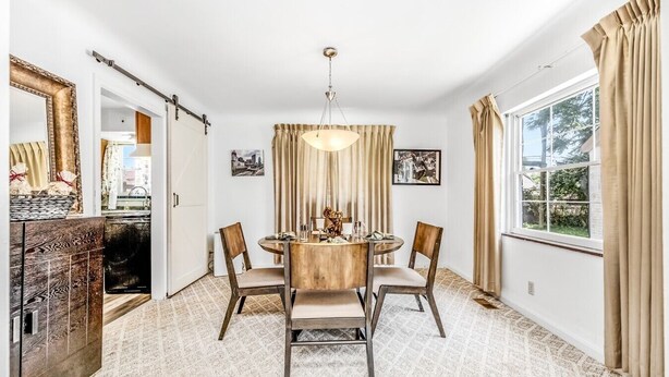 Un coin repas comprenant une table ronde, quatre chaises, un lustre et une fenêtre avec des rideaux.