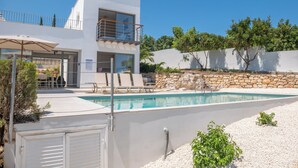 Et moderne hus med to etager, swimmingpool, udendørs møbler og en stenvæg.