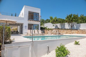 Ein modernes, zweistöckiges Haus mit Swimmingpool, Sitzgelegenheiten im Freien und einer Steinmauer.