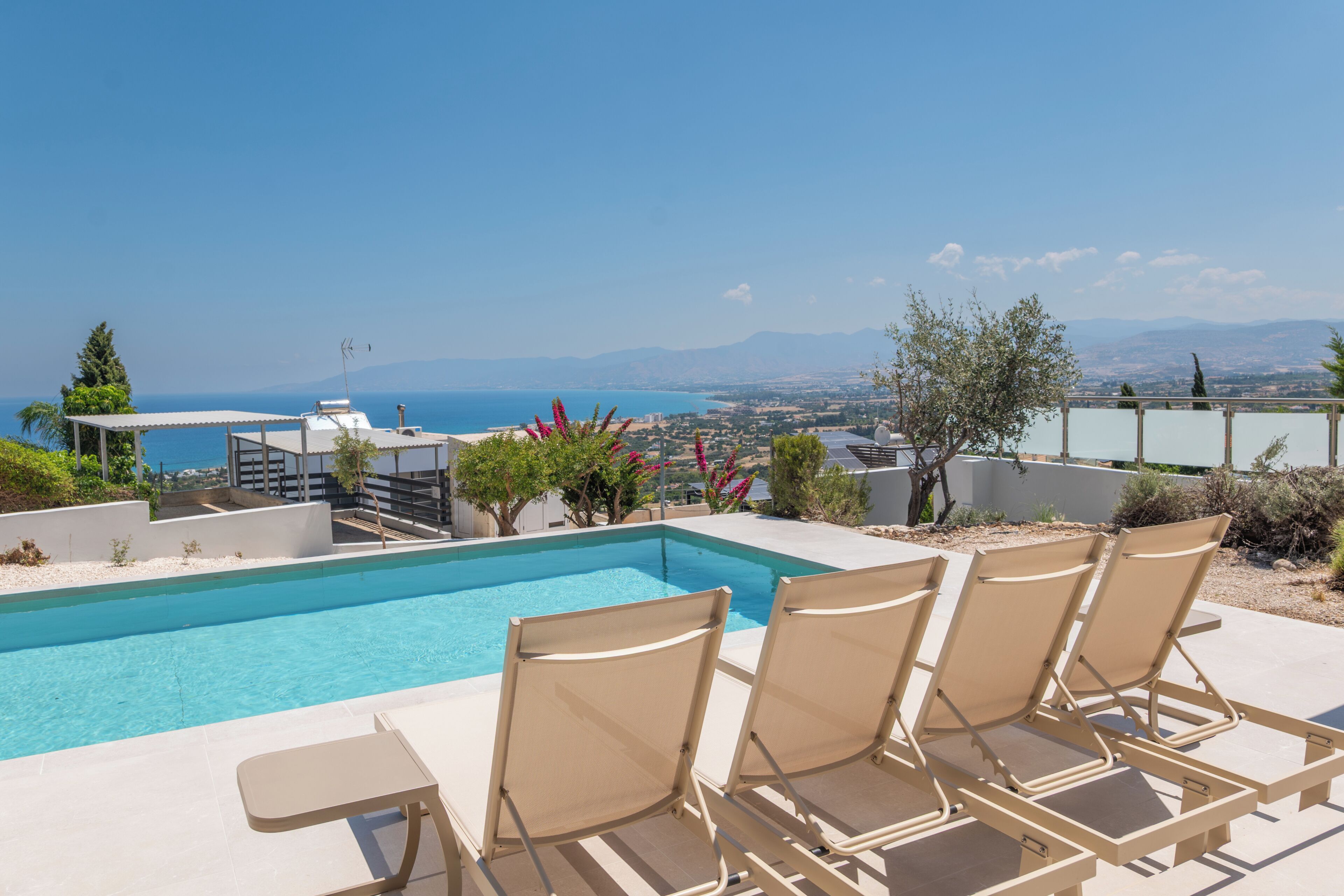 A pool area with lounge chairs and a view of the sea and mountains.