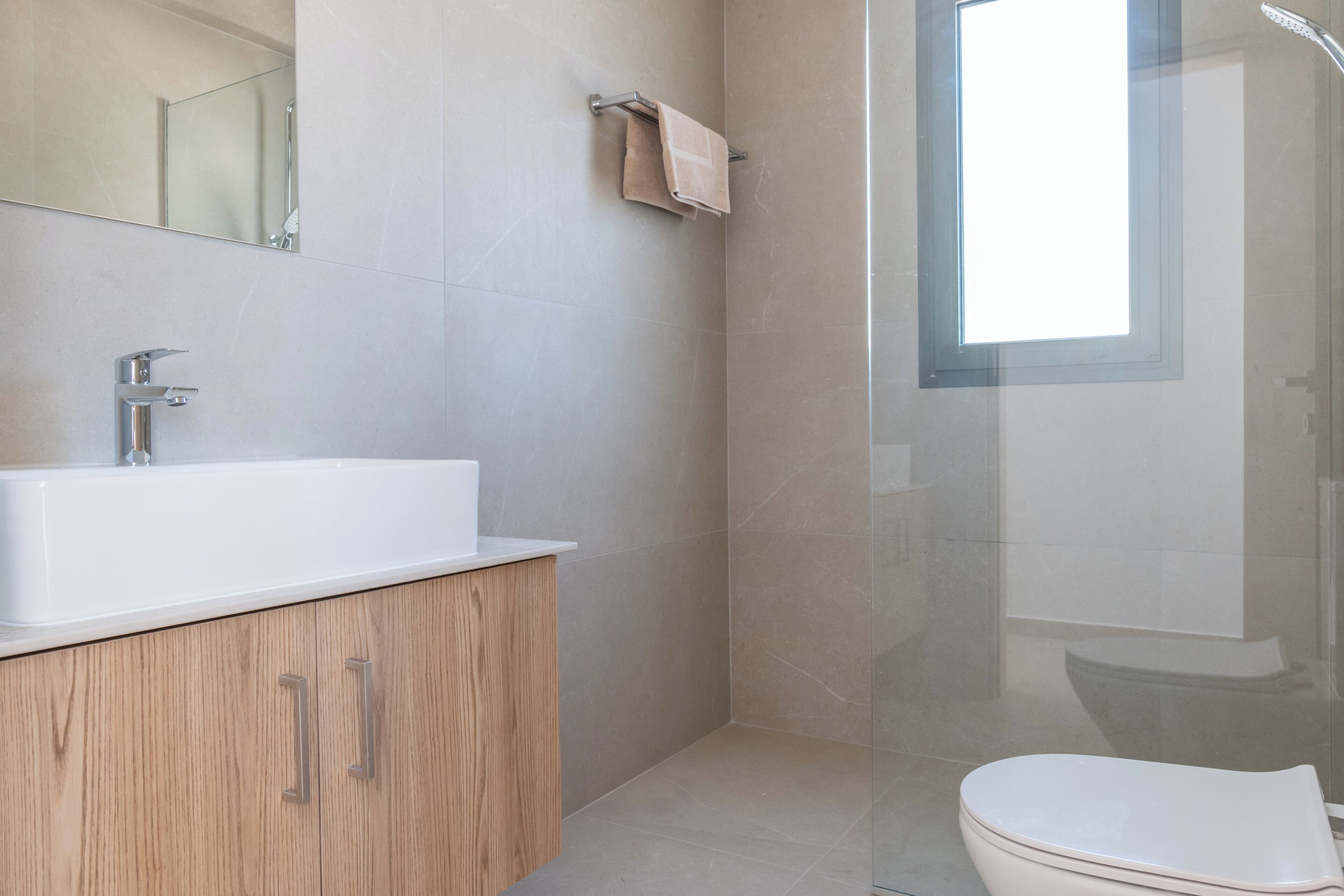 A modern bathroom with a white sink, wooden cabinet, and a glass shower enclosure.