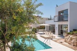 Ein modernes Gebäude mit Pool, Liegestühlen und einem Baum.