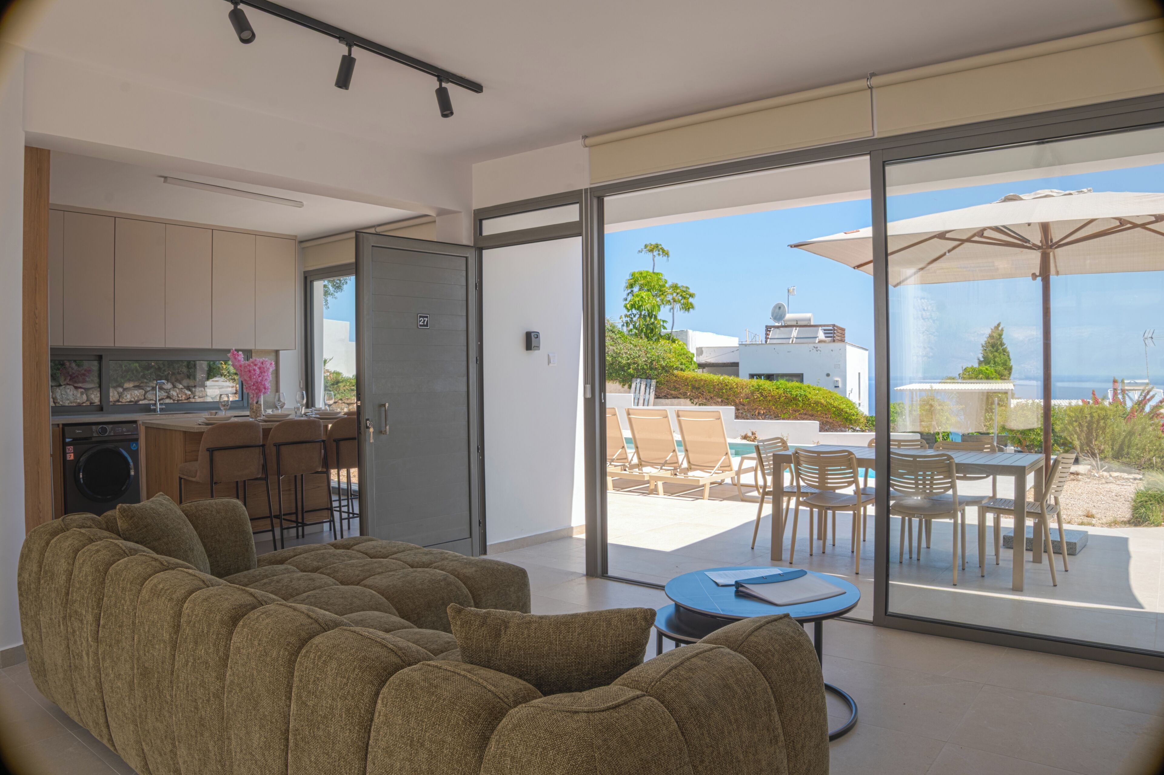 A modern living room with a sofa, a dining area with chairs and a table, and a kitchen with a washing machine.